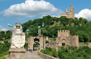 View of Tsarevets Fortress in Veliko Tarnovo, Bulgaria, with a stone lion statue and the Bulgarian flag in the foreground—perfect for guests staying at a local guest house or exploring nearby attractions such as Muddy Puddles Farm.